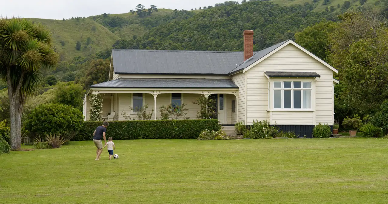 Landlord insurance in New Zealand, on a cream weatherboard rental home with a parent and small child on the front lawn.