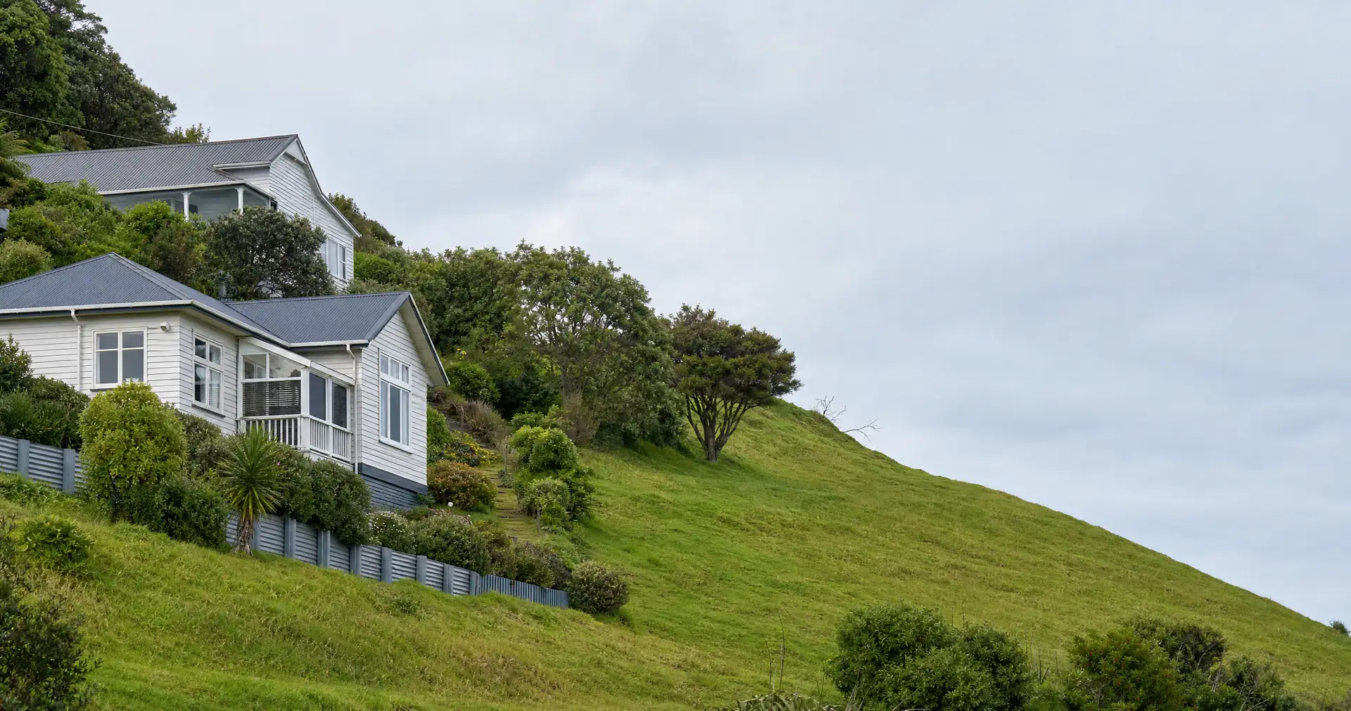 Weatherboard houses stepping up a steep green hillside, with retaining walls and trees between them.