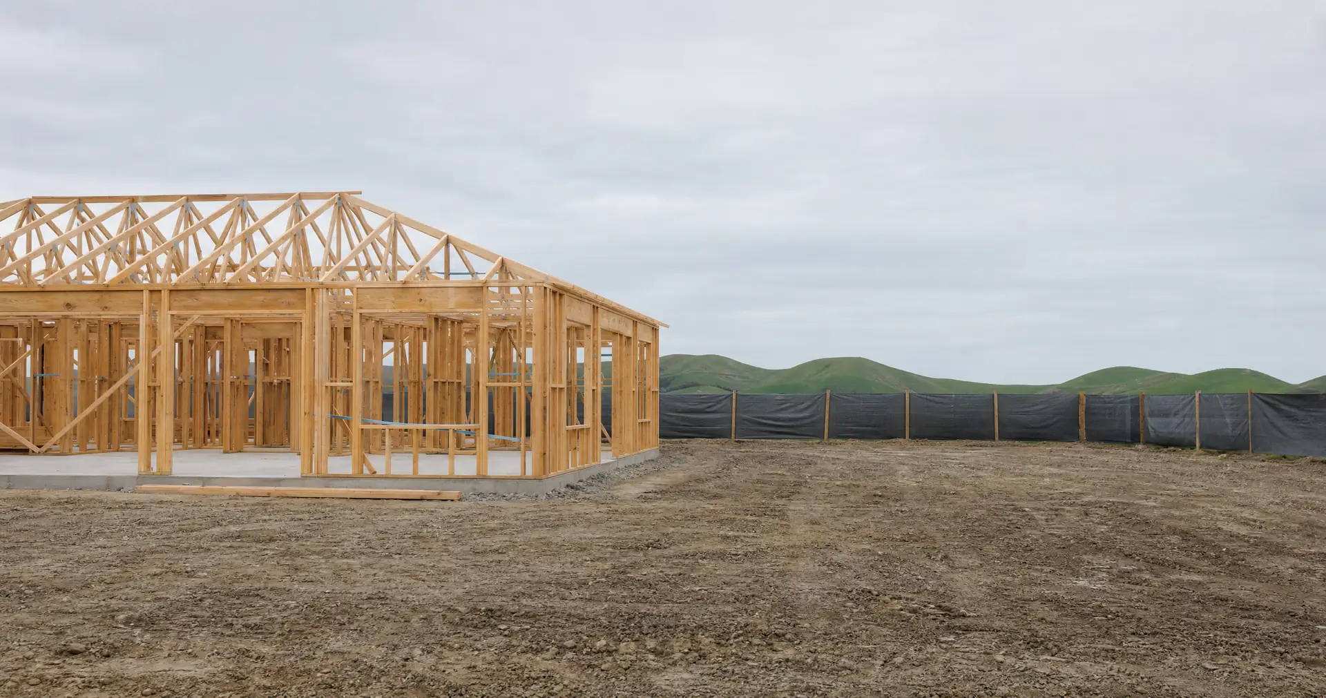 A house under construction, with fresh timber wall framing and new roof trusses on a concrete slab.